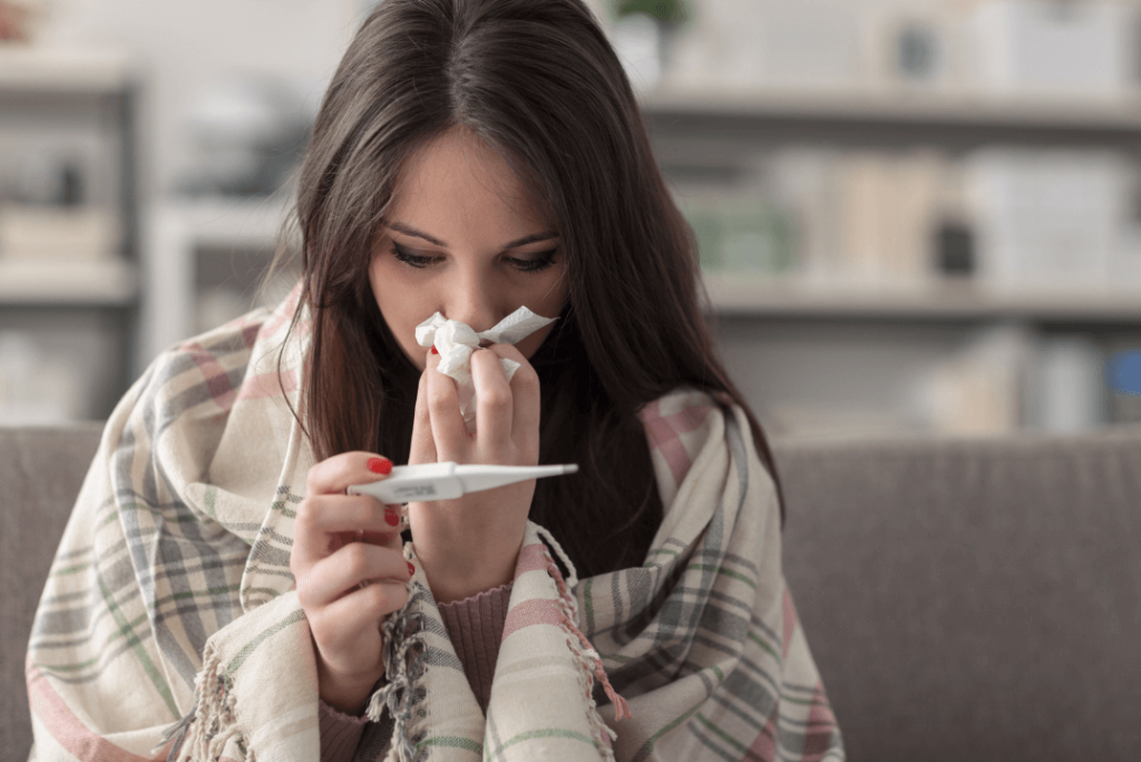 sick woman in blanket blowing nose looking at thermometer