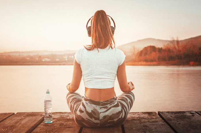 woman in camo yoga pants sitting on dock meditating with headphones