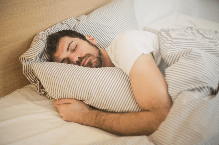 man sleeping soundly in bed with striped bedding and white sheets